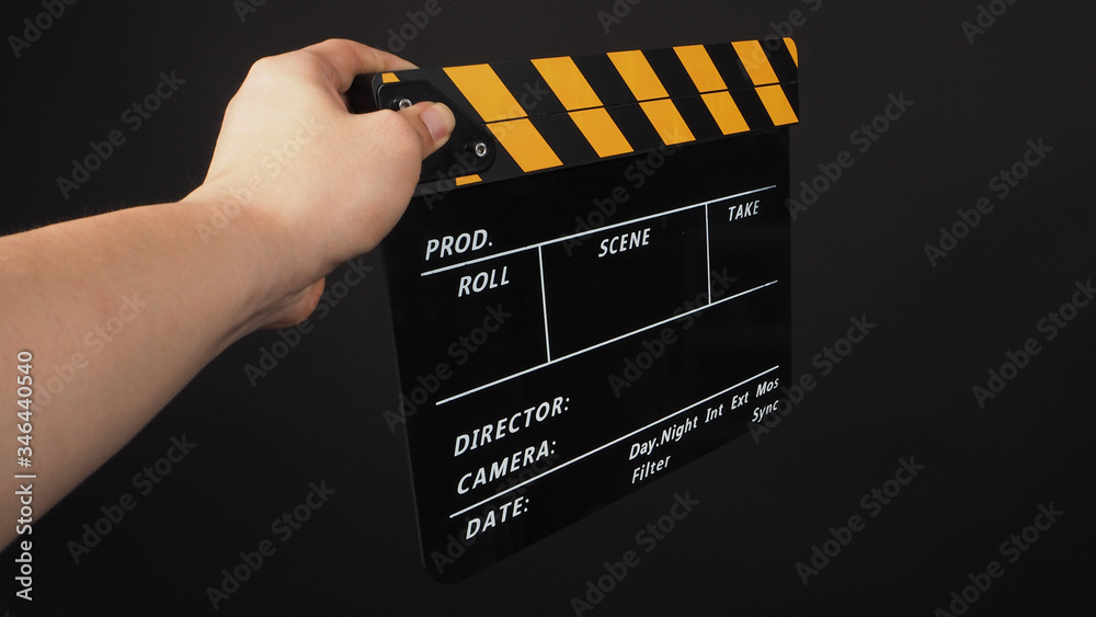 Hand is holding yellow and black color clapper board or movie slate on black background.