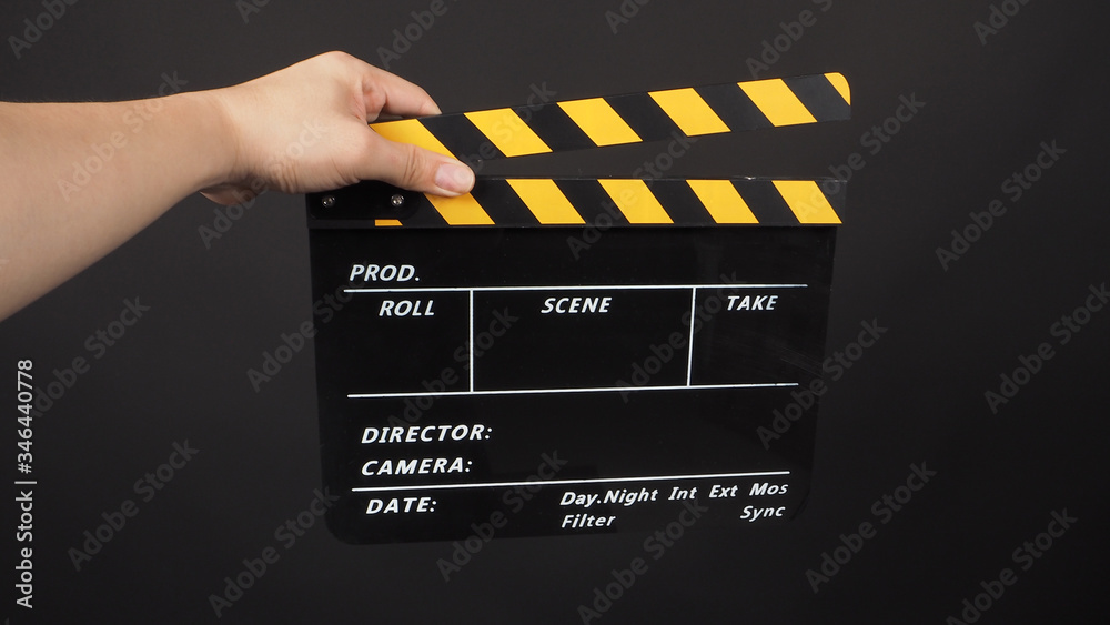 Hand is holding yellow and black color clapper board or movie slate.It is used in video production and film industry on black background.