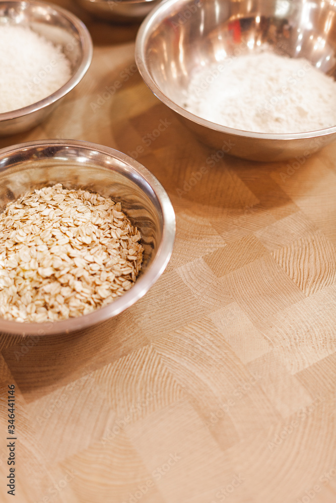 Metal bowls with oatmeal, flour and sugar on a wooden table Metal bowls with oatmeal, flour and sugar on a wooden table
