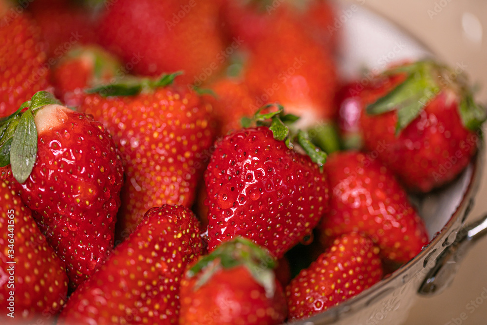 Ripe strawberries in white colander standing under pouring water in sink Ripe strawberries in white colander standing under pouring water in sink