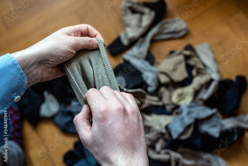 Heap of old socks as a symbol of old life, clutter, fast fashion, consumerism and nostalgic past. Male hands holding an old sock. Concept of tidying the mess