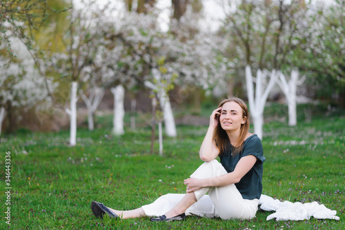 Girl looking into camera, sitting in a garden, when blossom cherry