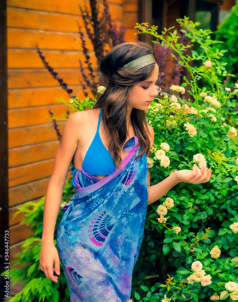 Beautiful young woman posing against a backdrop of greenery and a bungalow with a blue tissue. Elegant girl with scarf and bijouterie enjoying at beach. Freedom and carefree concept, Bali. tanning Beautiful young woman posing against a backdrop of greenery and a bungalow with a blue tissue. Elegant girl with scarf and bijouterie enjoying at beach. Freedom and carefree concept, Bali. tanning