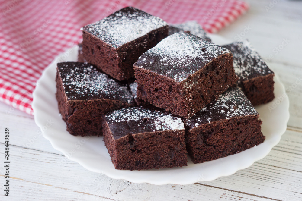 Chocolate cake cut into square pieces, sprinkled with icing sugar on a plate, white background Chocolate cake cut into square pieces, sprinkled with icing sugar on a plate, white background