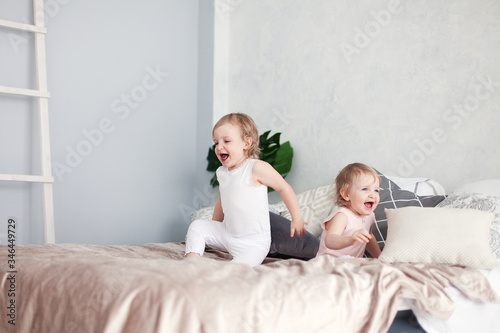 little blond sisters jump on the bed in the bedroom and laugh