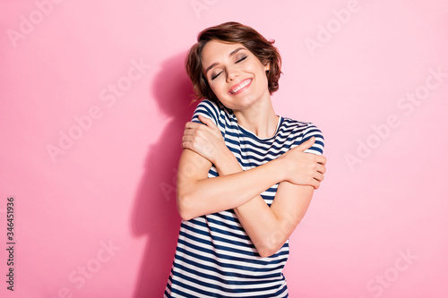 Photo of pretty nice sweet lady holding arms on shoulders hugging herself overjoyed eyes closed wear casual white blue t-shirt isolated pastel pink color background