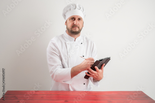 Young male chef in white uniform takes notes photo