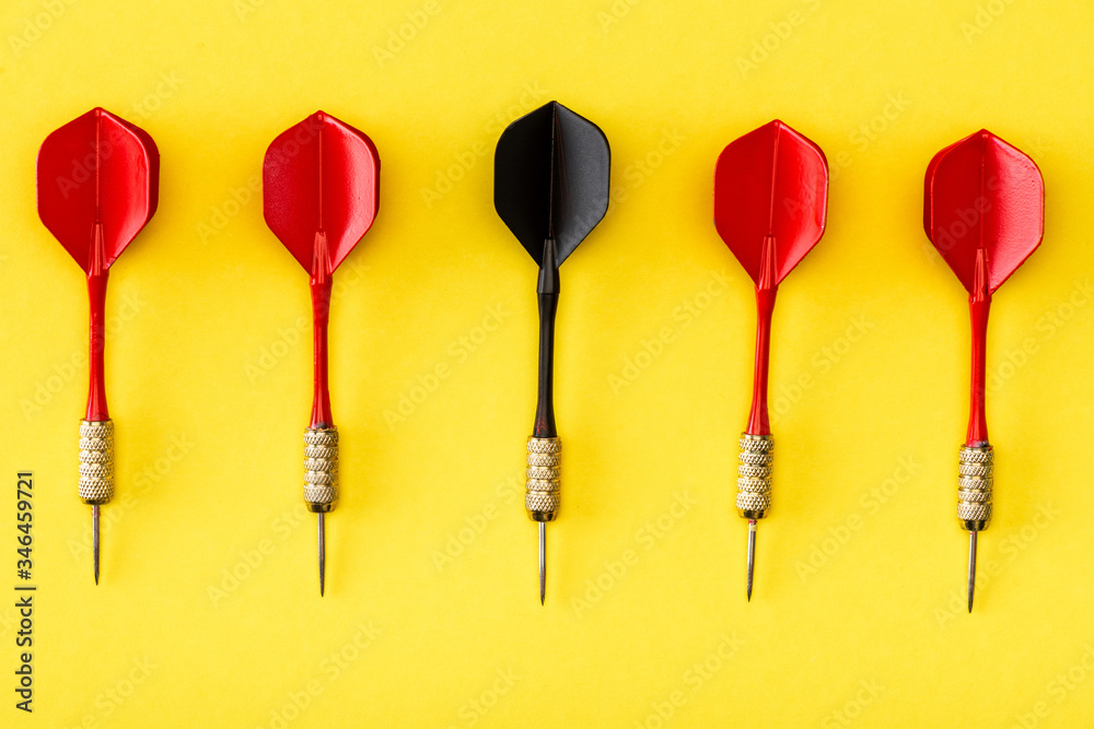 Flat lay with black dart among red on yellow Flat lay with black dart among red on yellow