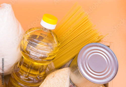 Donation box with food: canned food, pasta, peas, millet, sugar, oil, cookies on an orange background. Top view. Food stock for quarantine isolation period.