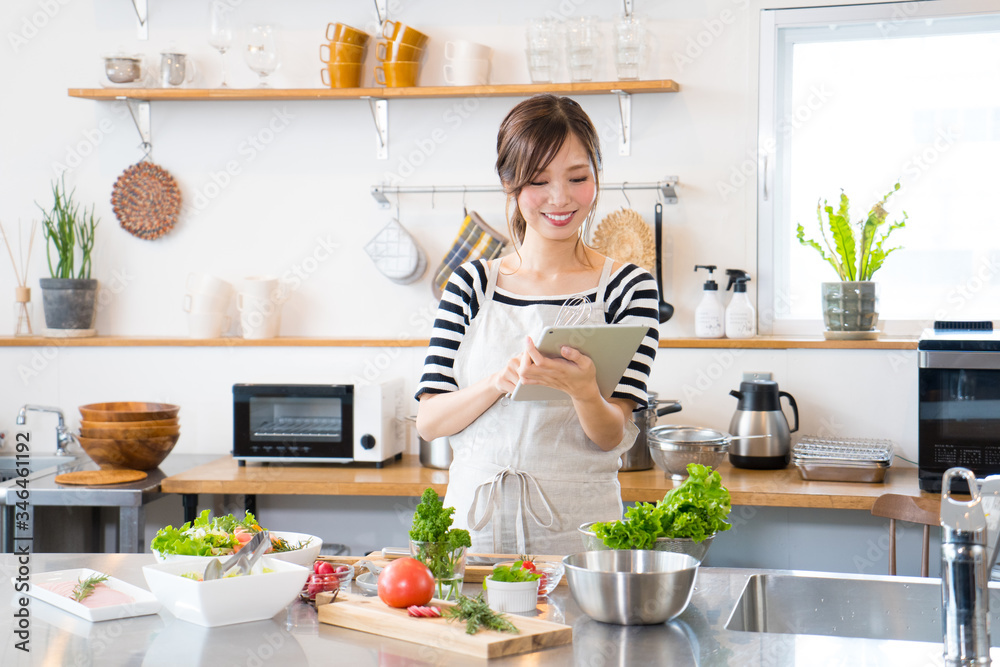 Φωτογραφία タブレットを見ながら料理を作る若い女性