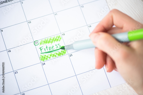 Cropped view of woman pointing with marker pen on fitness lettering in to-do calendar on wooden background