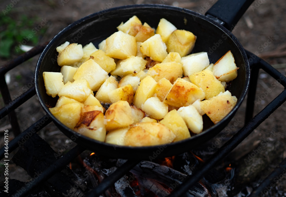 Potatoes are fried in a pan mounted on a wire rack over a fire. Potatoes are fried in a pan mounted on a wire rack over a fire.