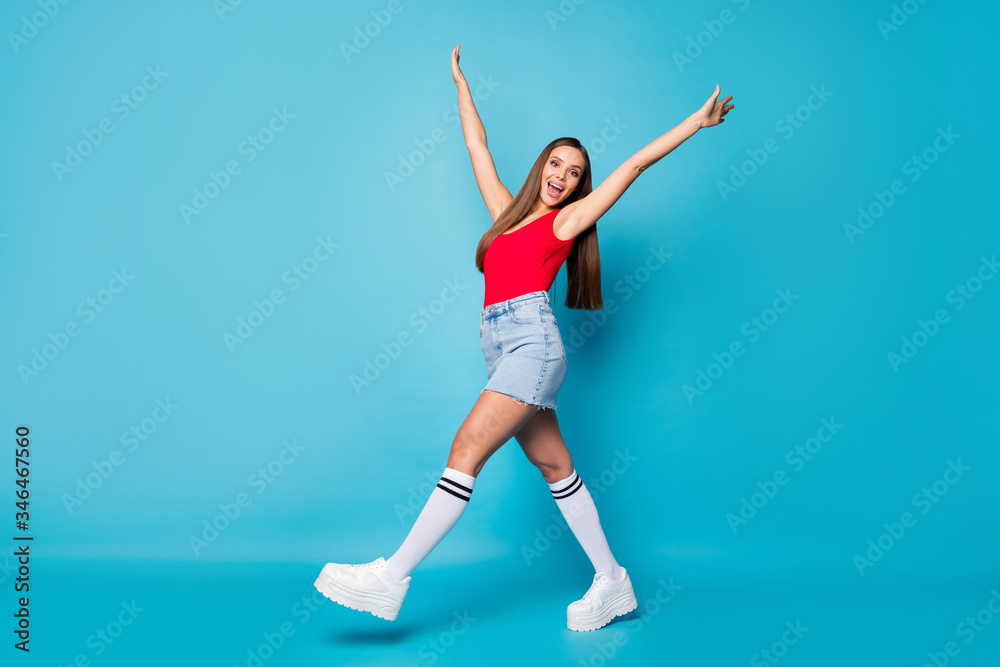 Full length profile side photo of excited cute lovely girl go walk enjoy spring weekend holiday raise hands wear casual style singlet footwear isolated over blue color background