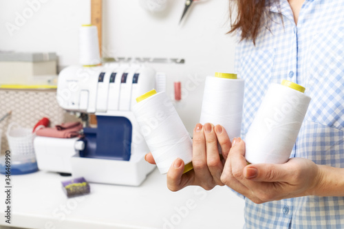 Sewing: an experienced girl, a dressmaker, holds large skeins of white thread in her hands and recommends using the correct type of thread with an overlock. photo