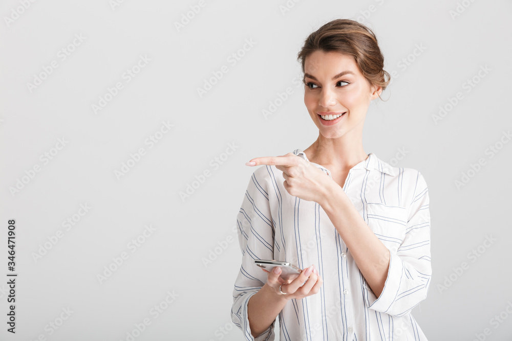 Image of joyful woman pointing finger aside and using cellphone Image of joyful woman pointing finger aside and using cellphone