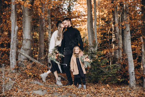 Stylish family in the autumn forest. A young guy and a girl are standing near a wooden fence with their daughter. Mom and daughter are holding bouquets of flowers