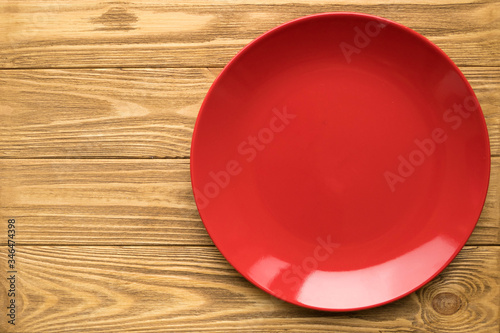 Empty red plate on a wooden table, top view