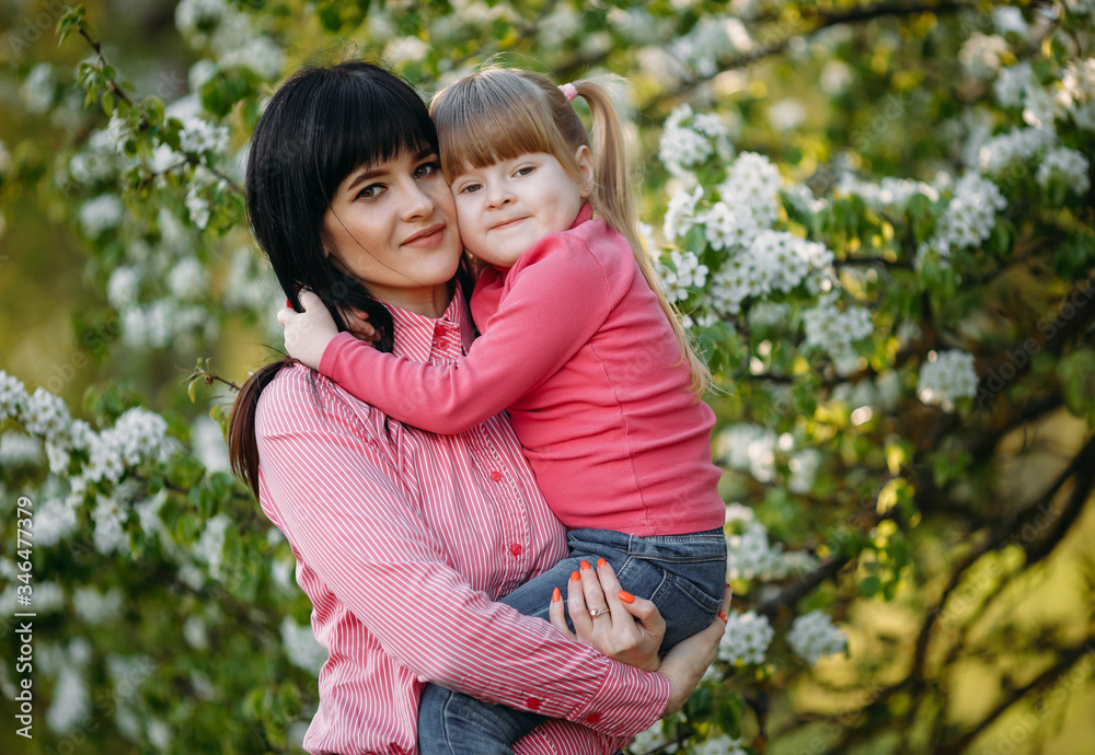 A little girl in her mother's arms in a park near a flowering tree