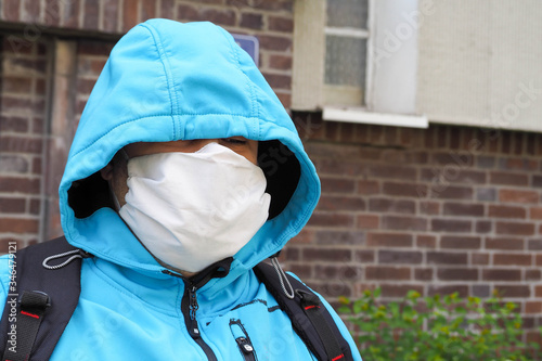 a light-skinned man in a blue jacket, hood, backpack and white face mask against the background of a brick house in the afternoon .during the coronavirus pandemic in Evropa .mask mode photo