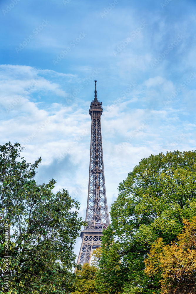 Eiffel Tower among the lush green trees against a bright blue cloudy sky. Vertical.