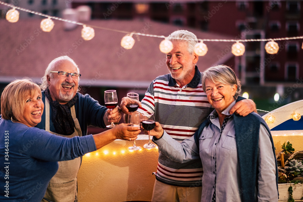 Happy group of old senior caucasian friends celebrate together by night clinking and toasting with red wine - end coronavirus emergency lokdown and people in friendship again free