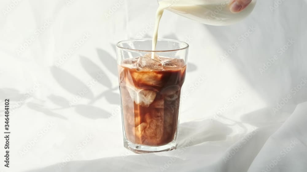 Milk cream is poured into a iced coffee cold brew. Coffee cold drink with ice and milk. Milk cream is poured into a iced coffee cold brew. Coffee cold drink with ice and milk.