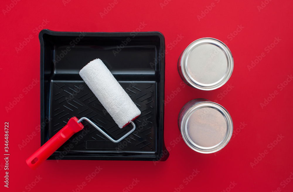 Obraz premium Paint roller, tray and two cans of paint on a red background. View from above. Concept