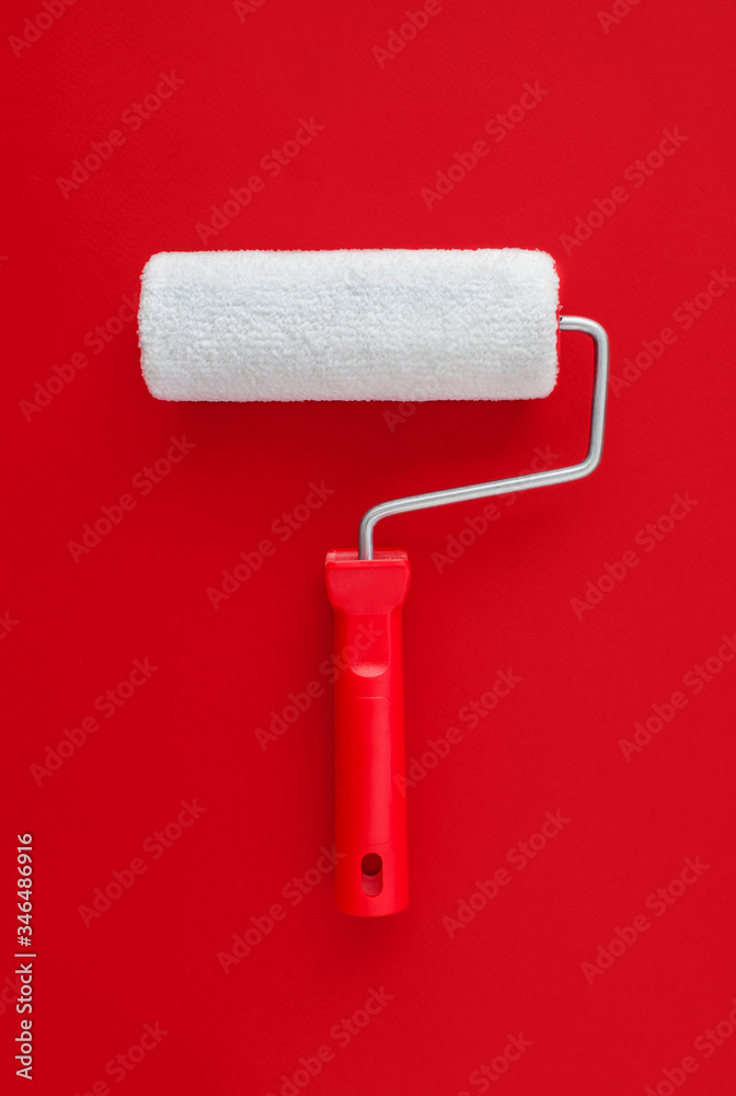 Obraz premium White paint roller with a red handle on a red background. Paint concept