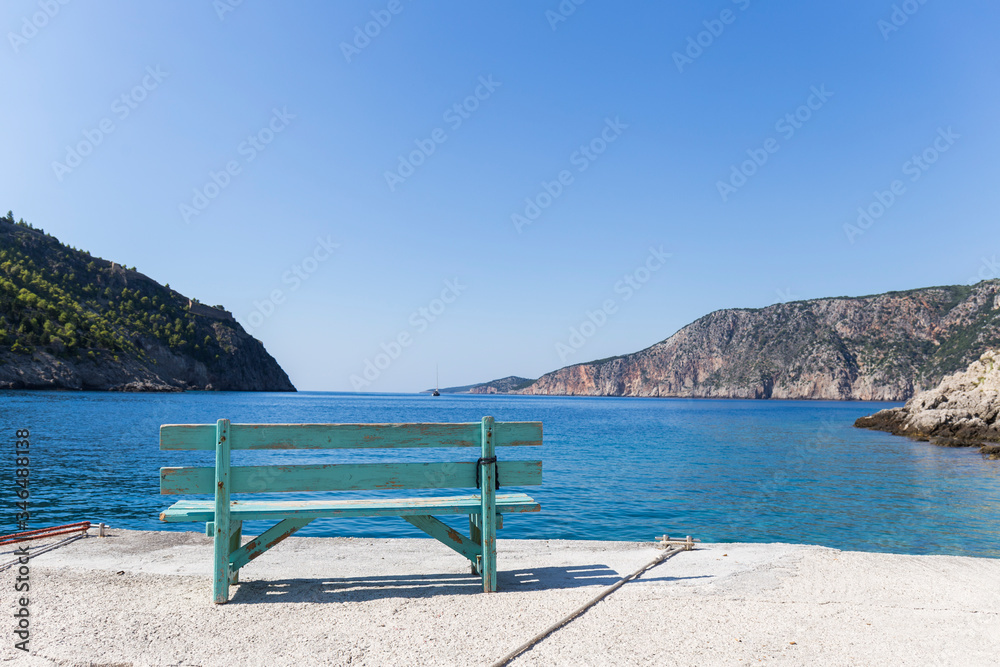 Turquoise wooden bench in sunny ocean view, facing beautiful mountains