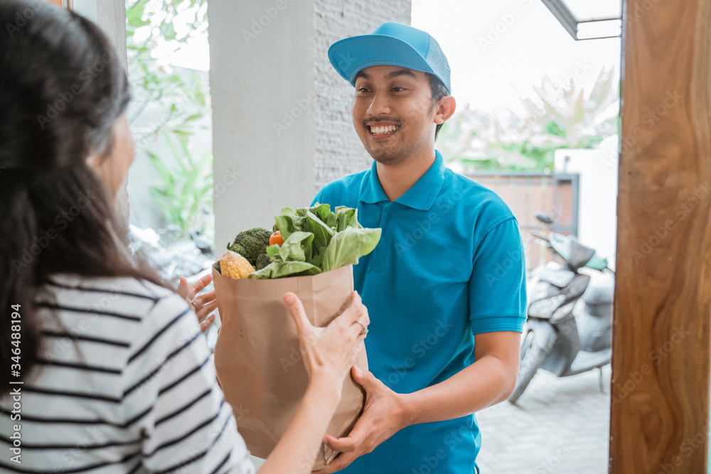 delivery boy is delivering some groceries to woman. He is handing her a shopping bag at her front door delivery boy is delivering some groceries to woman. He is handing her a shopping bag at her front door