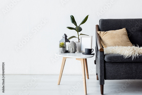 modern sofa with pillow near coffee table with plants, vintage lamp and cup in living room