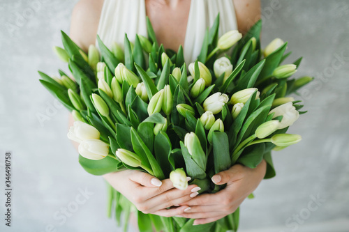 a bouquet of white tulips in the hands of a girl, a large beautiful armful of green leaves
