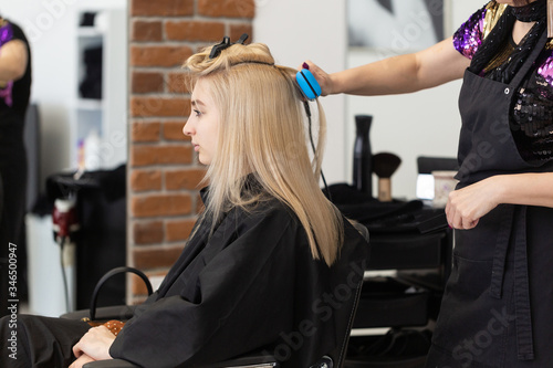 Beautiful blonde girl with long straight hair sits in a chair in a beauty salon. A professional hairdresser does the girl styling after dyeing hair. The girl is pleased with the care.