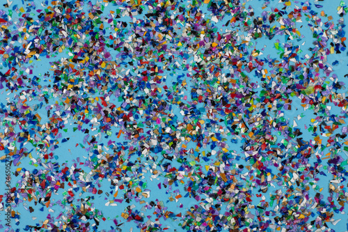 Circular crushed plastic pellets, parts made of multicolored recycled plastics collected at sea flatlay spread on a blue background to be used for new products. Waste particles, pollution reduction