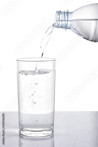 Pouring water from bottle into glass on white background with clipping path.
