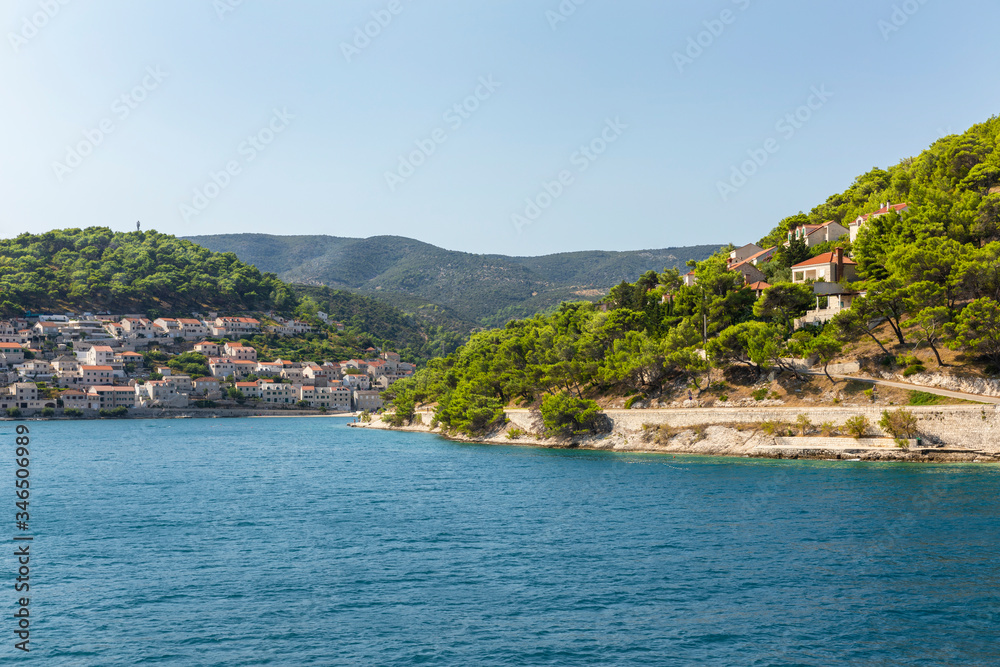 Pucisca town at Brac in Croatia, view from the sea on a sunny day in the summer. The port with it’s famous limestone from the island. Beautiful landscape, white stone creating a beautiful scenery