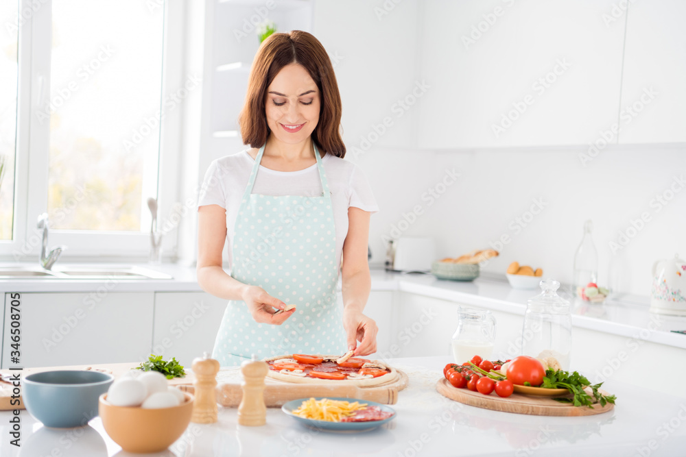 Photo of beautiful cheerful housewife quarantine hobby preparing family recipe mushroom slices on dough italian pizza stay home safety concept modern kitchen indoors