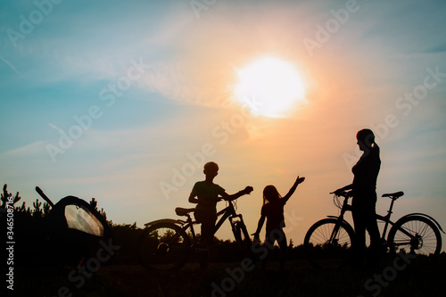 Happy mother with kids biking at sunset, family exercise in nature
