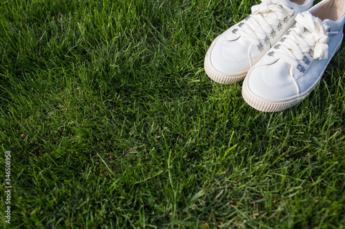 White women's sneakers on green grass on a sunny day.
