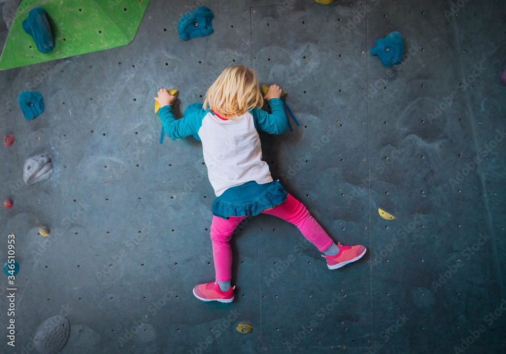 Fototapeta premium Little girl climbing on artificial boulders wall in gym