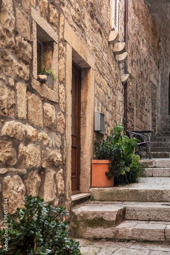 Fototapeta Naklejka Na Ścianę i Meble -  Narrow old Mediterranean street with stairs in Korcula. Rough stone houses and facades, green plants, flowers in Dalmatia, Croatia. Historical place creating a picturesque and idyllic scenery
