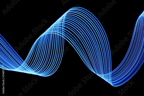 Long exposure photograph of neon electric blue colour in an abstract swirl, parallel lines pattern against a black background. Light painting photography.