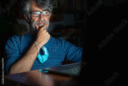 middle-aged man looks at the computer news about the global pandemic of the crown virus, analyzes perplexed information, conspiracy hypothesis about the epidemic, concern for business and health photo