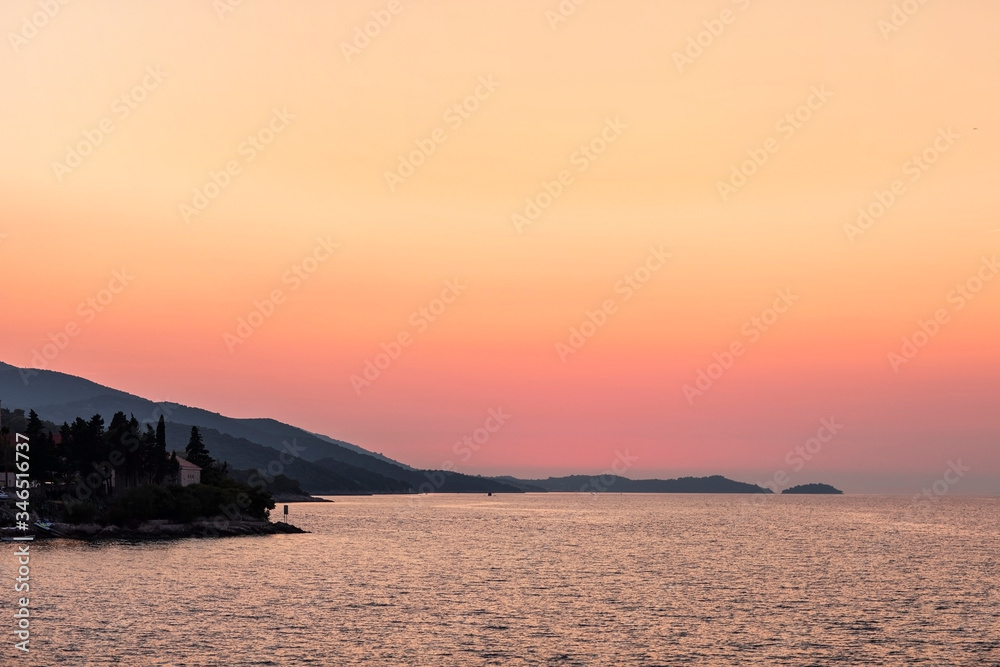 Korcula island shot from the sea during sunset in summer. Beautiful old venetian town with mountains and a orange and red sky with deep pink colors creating an idyllic scenery. Holiday destination