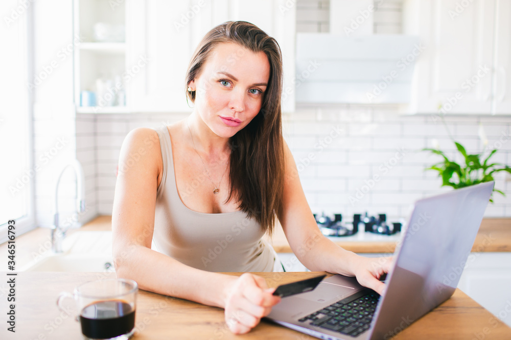 Woman holding black credit card and typing somethingon a laptop staying at the kitchen. Online shopping, stay at home concept Woman holding black credit card and typing somethingon a laptop staying at the kitchen. Online shopping, stay at home concept