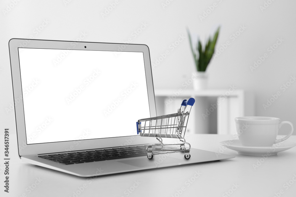 Online shopping. Laptop with small cart and cup on table Online shopping. Laptop with small cart and cup on table