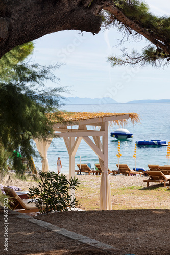 Fototapeta Naklejka Na Ścianę i Meble -  Bol on Brac island view with beach beds and sun umbrella’s. A path near the sea on a sunny day in summer in Dalmatia, Croatia. Clear blue Adriatic water at the Mediterranean coast. Idyllic scenery