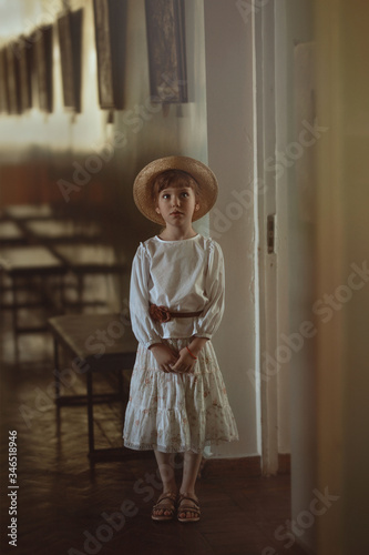 girl in a straw hat and retro clothes stands in the hallway of an old building