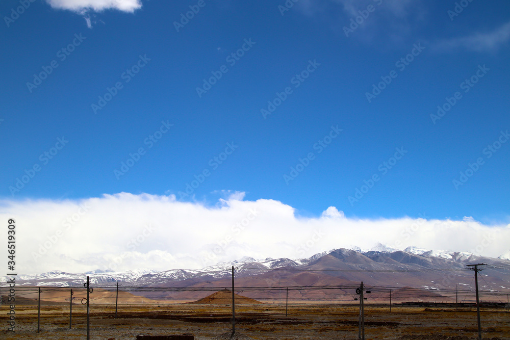 The magnificent scenery of the Everest Scenic Area, the brown hillside, the snowy mountains in the distance, the blue sky and white clouds, the road to the distance