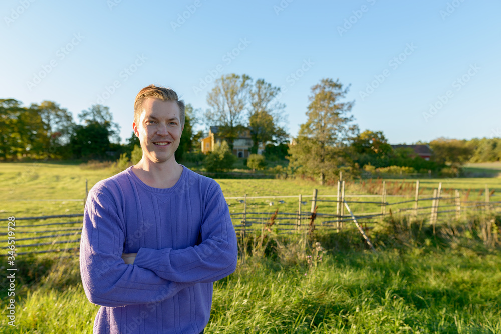Happy young man smiling with arms crossed in peaceful grassy plain with nature